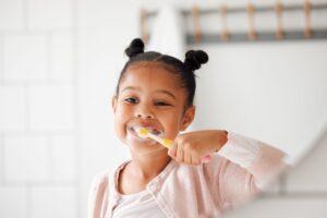 Little girl brushing teeth in white tiled bathroom